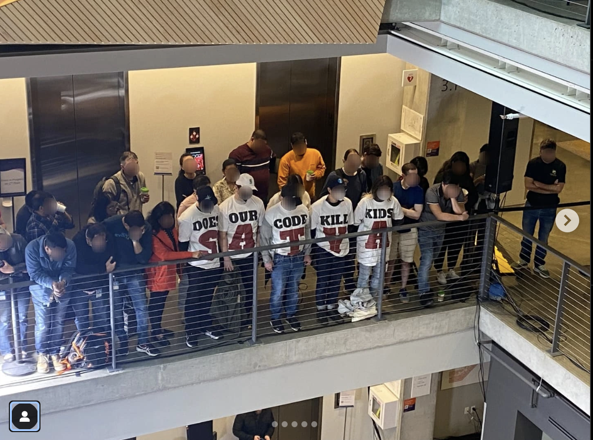 Five workers standing in the midst of other workers with text on their tee-shirts saying, collectively "Does our code kill kids, Satya?"